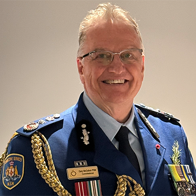 A headshot of CSNSW Commissioner Gary McCahon PSM in uniform in front of ceremonial flags