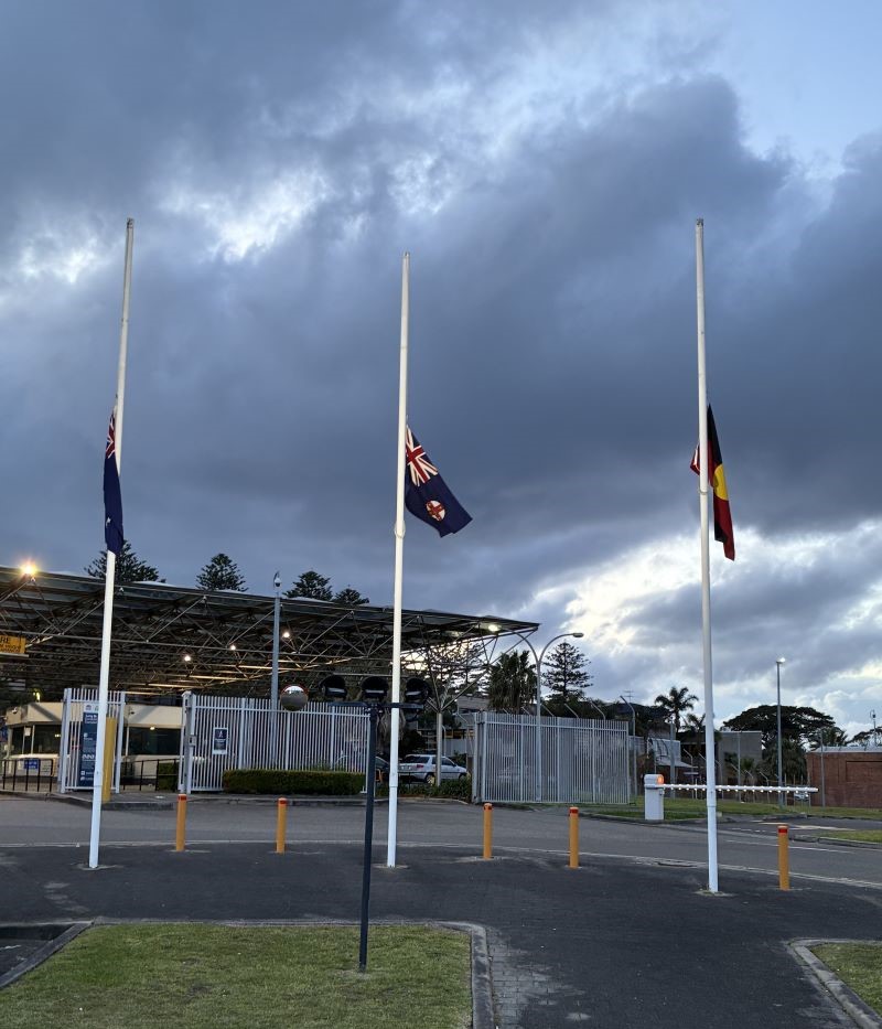 Gatehouse of Long Bay jail in background, NSW and indigenous flag flying at half mast in foreground