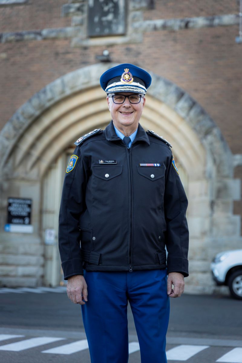 Man in Commissioner's hat standing in front of sandstone building.
