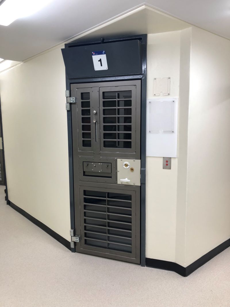 A cell door, with grills at the top and bottom and a slot in the middle for a food tray