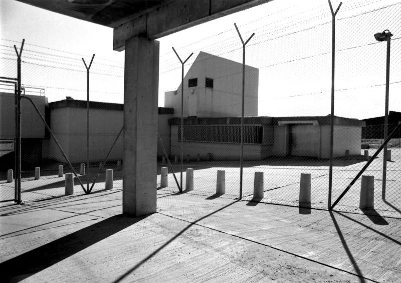 black and white photograph of concrete excercise yard hemmed in by high barbed wire security fence
