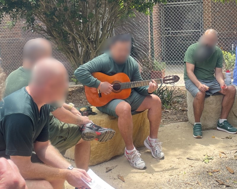 Men sitting in a circle and one is playing a guitar